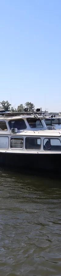 Een zwarte boot met de naam "Don Pancho" vaart op het water, met een jachthaven op de achtergrond.