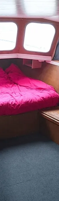 De foto toont het interieur van een boot met een bed met roze dekbed, ramen, gordijnen en een brandblusser.