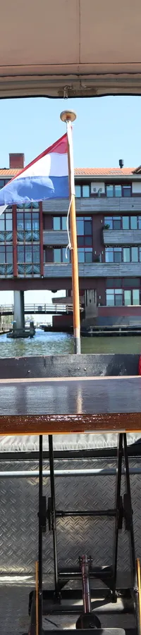 Een bootinterieur met een houten tafel, twee banken met grijze kussens en twee rode kussens, met uitzicht op een gebouw en…