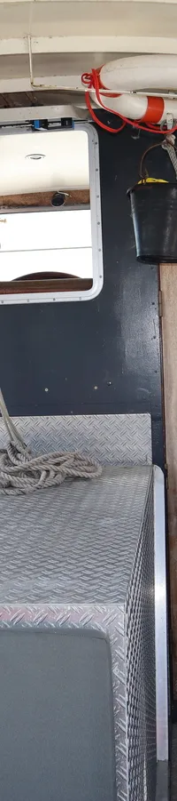 De foto toont het interieur van een boot met houten deuren, ramen, een reddingsboei en een touw op een metalen oppervlak.