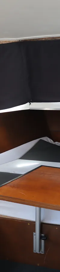 De kajuit van een boot met een houten tafel, banken met kussens, en zwarte gordijnen voor de ramen.