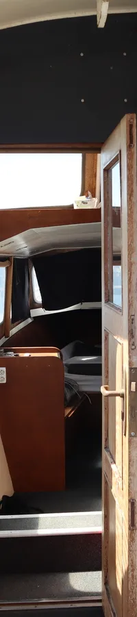 Een interieur van een boot met een open deur naar een kajuit, een metalen vloer en uitzicht op een haven.