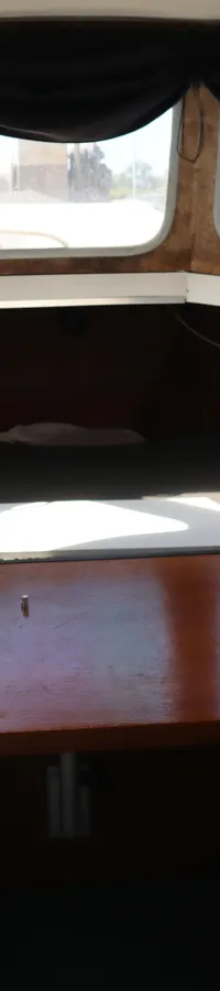 De kajuit heeft een houten interieur met een tafel in het midden, banken aan de zijkanten en ramen met zwarte gordijnen.