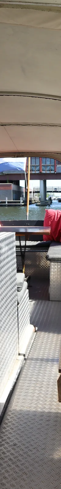 Een interieur van een boot met een houten deur, een brandblusser, een bankje met rode kussens en een trapje.