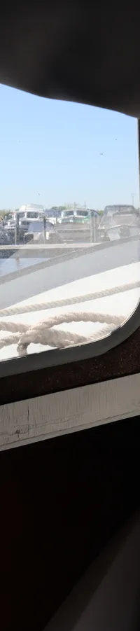De foto toont het interieur van een boot met uitzicht door de ramen op een jachthaven met andere boten.