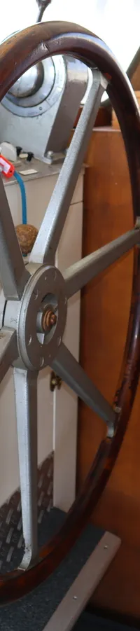 Een houten stuurwiel met metalen spaken staat voor een wit bedieningspaneel met diverse meters en schakelaars.