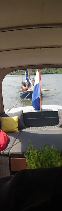 Een boot met een beige kap en doorzichtige zijpanelen vaart op een waterweg, met een andere boot in de verte.