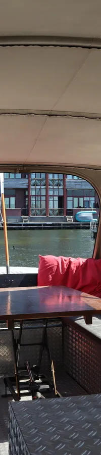 De foto toont het interieur van een boot met een beige kap, banken, een tafel en rode kussens. — WSA vlet Ex patrouille boot