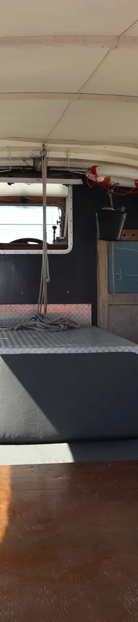 De foto toont het interieur van een boot met een houten tafel, banken, en een canvas dak met doorzichtige zijpanelen.