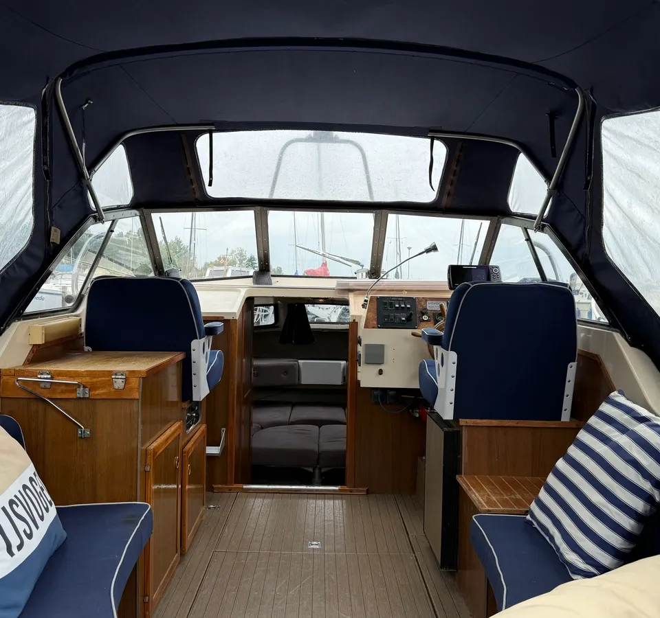 De foto toont het interieur van een boot met een donkerblauwe kap, twee stuurstoelen en een houten vloer. — Joda 7500