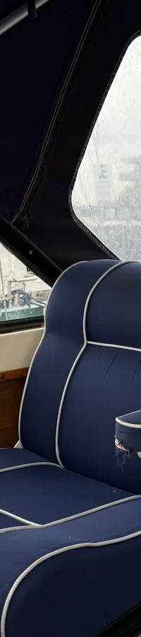 Een blauwe bootstoel met witte biezen en een blauwe bank met kussens zijn zichtbaar in een bootinterieur.