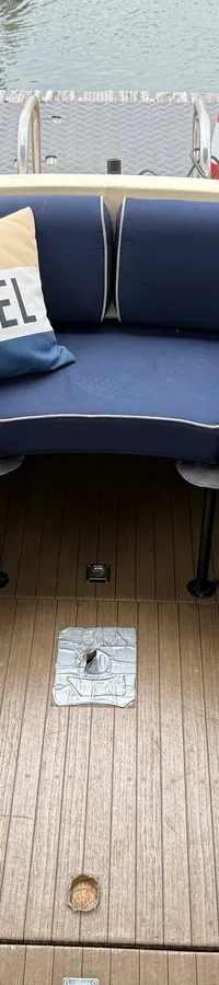 Een bootinterieur met een U-vormige zithoek met donkerblauwe kussens, twee kussens met de tekst "IJSVOGEL" en een gestreept…