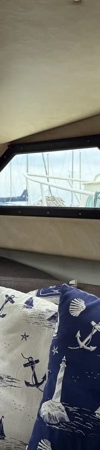 De foto toont het interieur van een boot met een bank, kussens en ramen die uitzicht bieden op andere boten. — Joda 7500