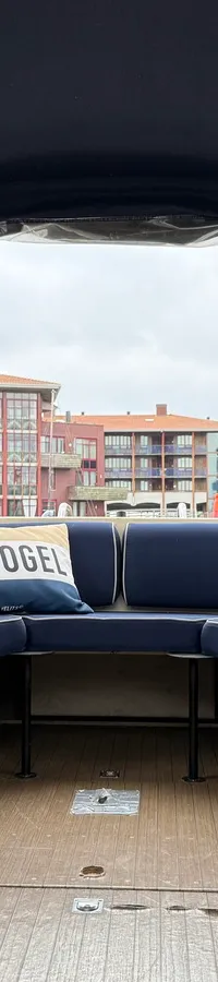 De foto toont het interieur van een boot met blauwe kussens, een kussen met "IJSVOGEL" erop, en houten details. — Joda 7500