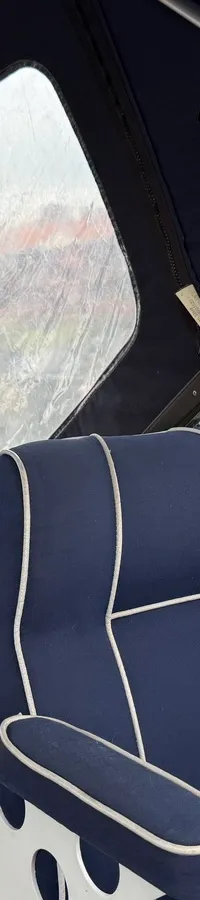 Een blauwe bootstoel met witte biezen en een blauwe bank met kussens, zichtbaar door een raam van een boot. — Joda 7500