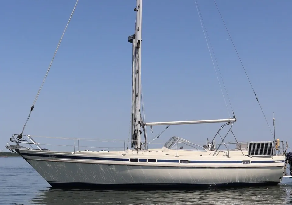 Een witte zeilboot met blauwe strepen op het water, met een buitenboordmotor en zonnepaneel aan de achterkant. — Contest 38S