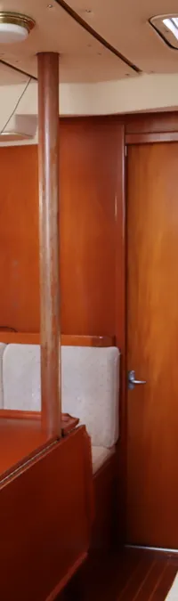 De foto toont het interieur van een boot met houten wanden, een bank met lichte kussens en een inklapbare tafel.
