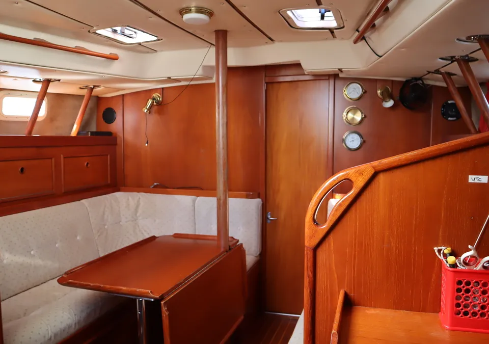 De foto toont het interieur van een boot met houten wanden, een bank met lichte kussens en een inklapbare tafel.