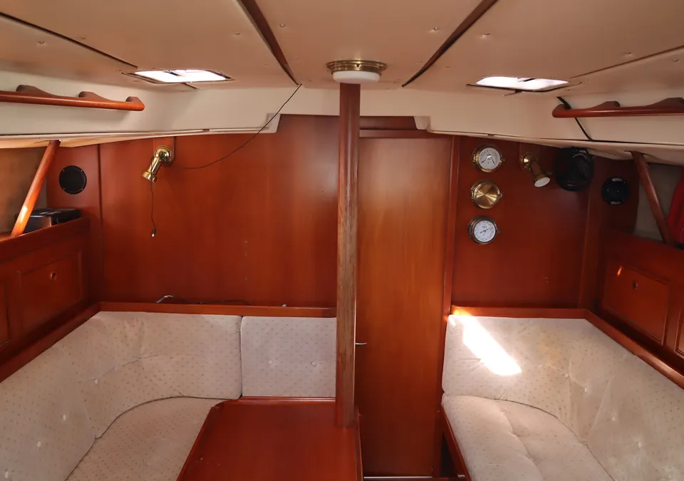 De foto toont het interieur van een boot met houten wanden, beige kussens en een tafel in het midden. — Contest 38S