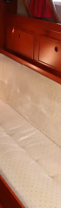 De foto toont een interieur van een boot met houten lambrisering, een bank met lichte kussens en een houten vloer.