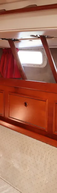 De foto toont een interieur van een boot met houten wanden, een bank met lichte kussens en patrijspoorten met rode gordijnen.