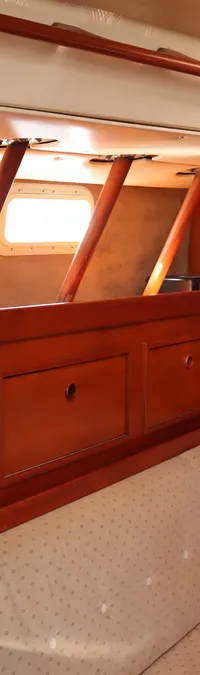 De foto toont een interieur van een boot met houten wanden, een bank met lichtgekleurde kussens en patrijspoorten.