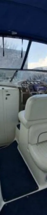 De foto toont het interieur van een boot met een blauwe kap, witte bekleding, een stuurstand, een wasbak en blauwe…