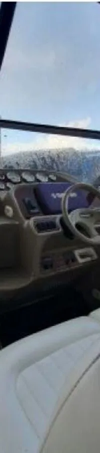 De foto toont het stuurstation van een boot met een wit stuurwiel, dashboard, witte bekleding en een voorruit met blauwe kap.
