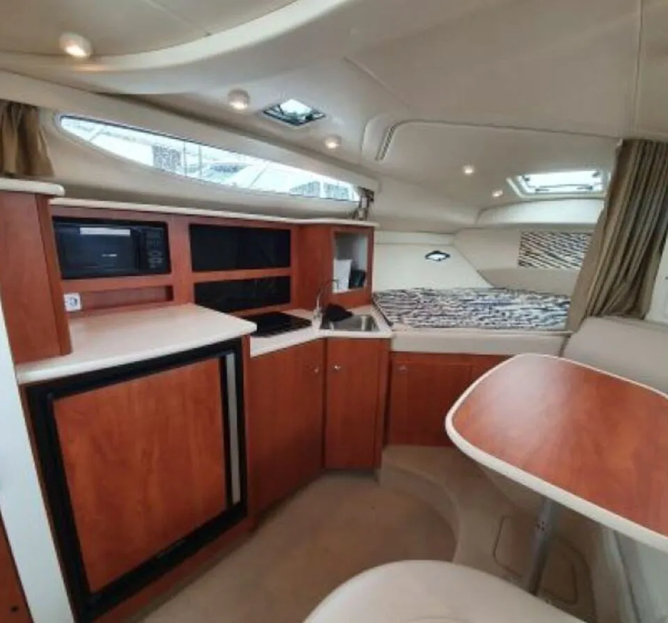 De foto toont het interieur van een bootkajuit met een kombuis, een V-kooi en een dinette.