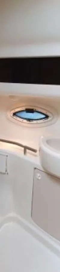 Een bootbadkamer met een toilet, wastafel met kraan, een spiegel, een patrijspoort en een langwerpig raam.