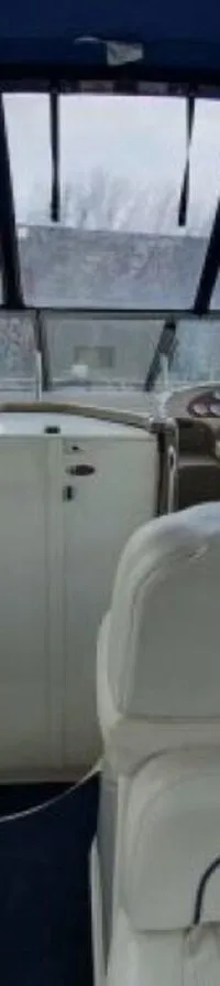 De foto toont het interieur van een boot met witte zitplaatsen, een stuurwiel, dashboard en een blauwe biminitop.