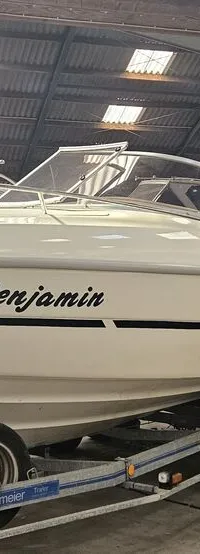 Een witte motorboot met de naam "Benjamin" op de zijkant staat op een trailer in een loods, naast een andere boot.