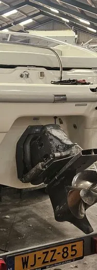 Een witte boot staat op een trailer in een loods, met de achterkant en de buitenboordmotor in beeld. — Cranchi 21 Ellipse