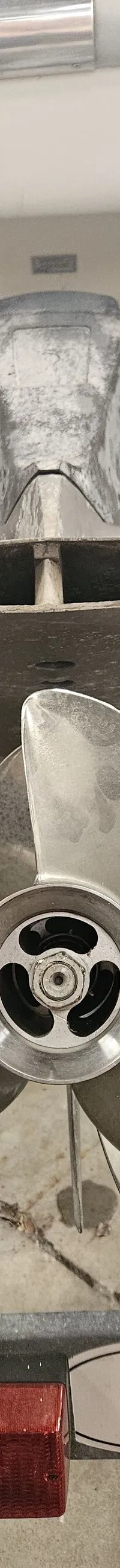 Een close-up van een buitenboordmotor met een driebladige schroef, gemonteerd op een boot die op een trailer staat.