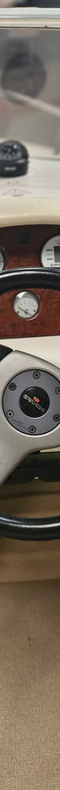 Een stuurwiel met een dashboard met meters en schakelaars, en een kompas op het voordek.