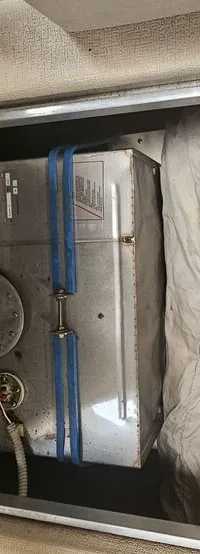 Een open opbergruimte met een metalen tank vastgezet met blauwe banden en een opgevouwen zeil met "ELLIPSE 21" erop.