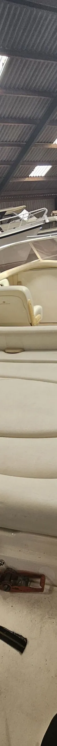 Een witte speedboot met beige bekleding staat in een opslagloods met andere boten en een golfplaten dak. — Cranchi 21 Ellipse
