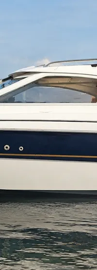 Een witte motorboot met een donkerblauwe streep en een gouden lijn vaart op rustig water. — Yamarin 68C