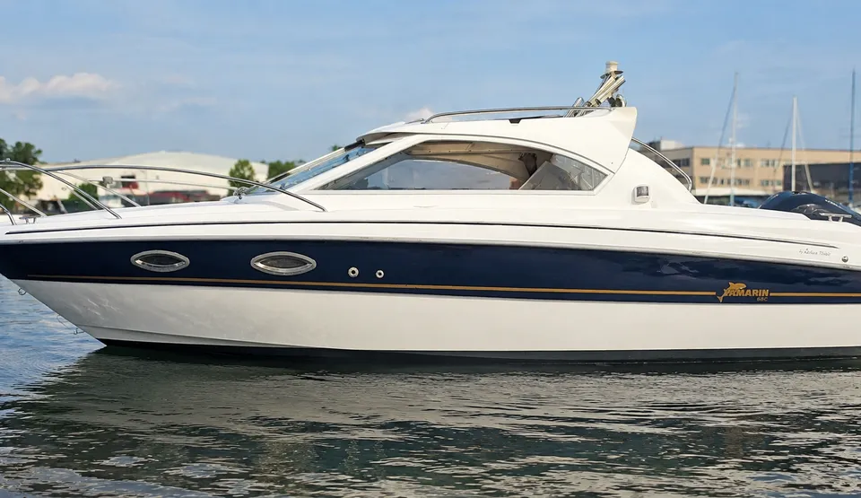 Een witte motorboot met een donkerblauwe streep en een gouden lijn vaart op rustig water. — Yamarin 68C