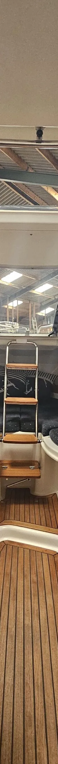 De foto toont het interieur van een boot met een stuurwiel, een Garmin-scherm, houten vloeren en blauwe kussens.