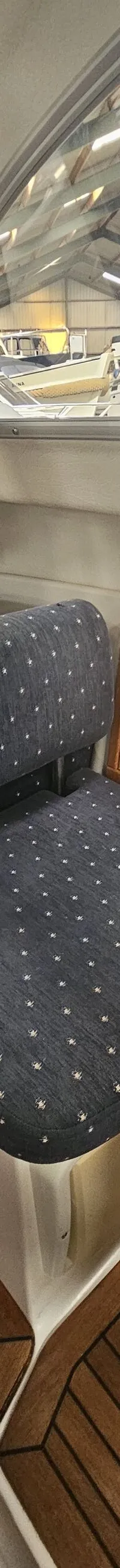 Een interieur van een boot met een donkerblauwe gestoffeerde stoel, een houten tafel en een raam met uitzicht op een loods.