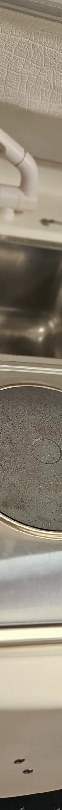 Een close-up van een scheepskombuis met een roestvrijstalen spoelbak, een kraan en een kookplaat.