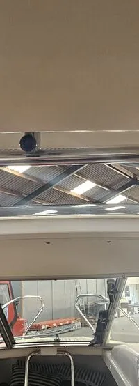 De foto toont het interieur van een boot met een open dak en een voorruit, met uitzicht op een loods met andere boten.
