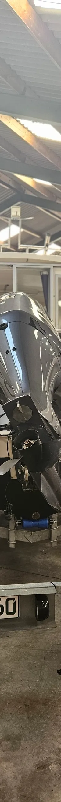 Een witte boot met een grijze buitenboordmotor staat op een trailer in een loods. — Yamarin 68C