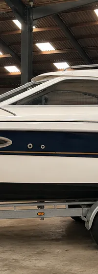 Een witte boot met een donkerblauwe streep en de naam "YAMARIN" staat op een dubbelassige trailer in een loods. — Yamarin 68C