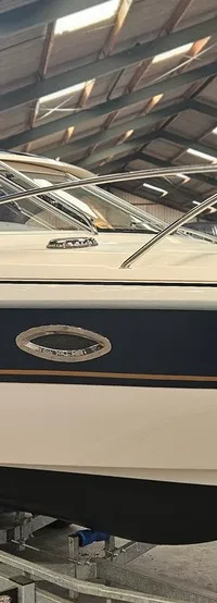 Een witte boot met een donkerblauwe streep en gouden accenten staat op een trailer in een loods. — Yamarin 68C