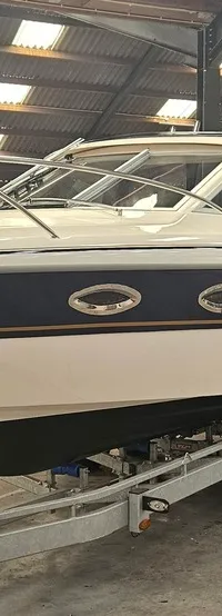 Een witte boot met een donkerblauwe streep en goudkleurige accenten staat op een trailer in een loods. — Yamarin 68C