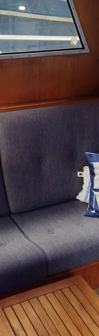 Een interieur van een boot met een grijze hoekbank, twee kussens met nautische thema's en een houten salontafel.