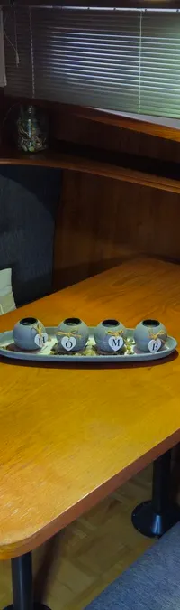 Een houten interieur van een boot met een eettafel, banken met grijze kussens, een raam met jaloezieën en decoratie.