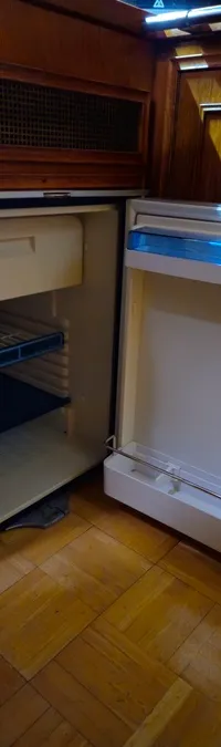 Een open koelkast met een vriesvak en een roosterplank, ingebouwd in een houten interieur met een houten vloer.